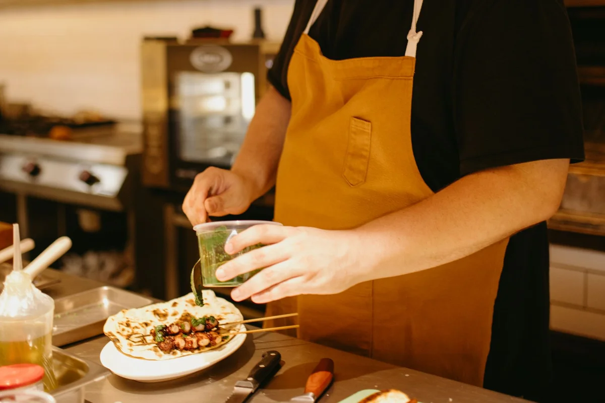 A chef in a warm kitchen finishing a plated meal